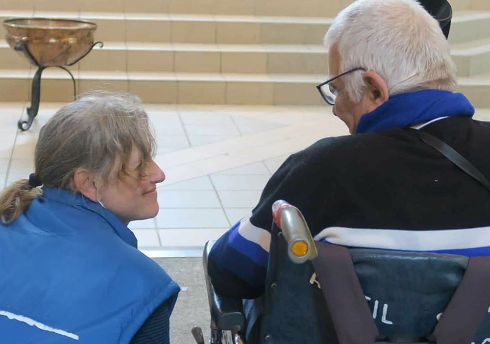 une dame porte assistance a une personne âgée en fauteuil roulant